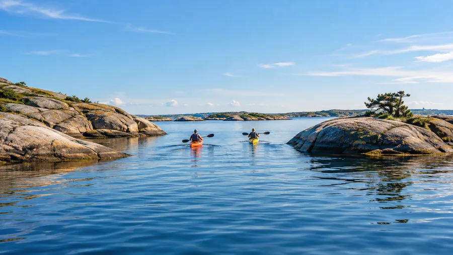 Dos kayaks de mar, uno naranja y otro amarillo, remando entre pequeñas islas de granito bajo